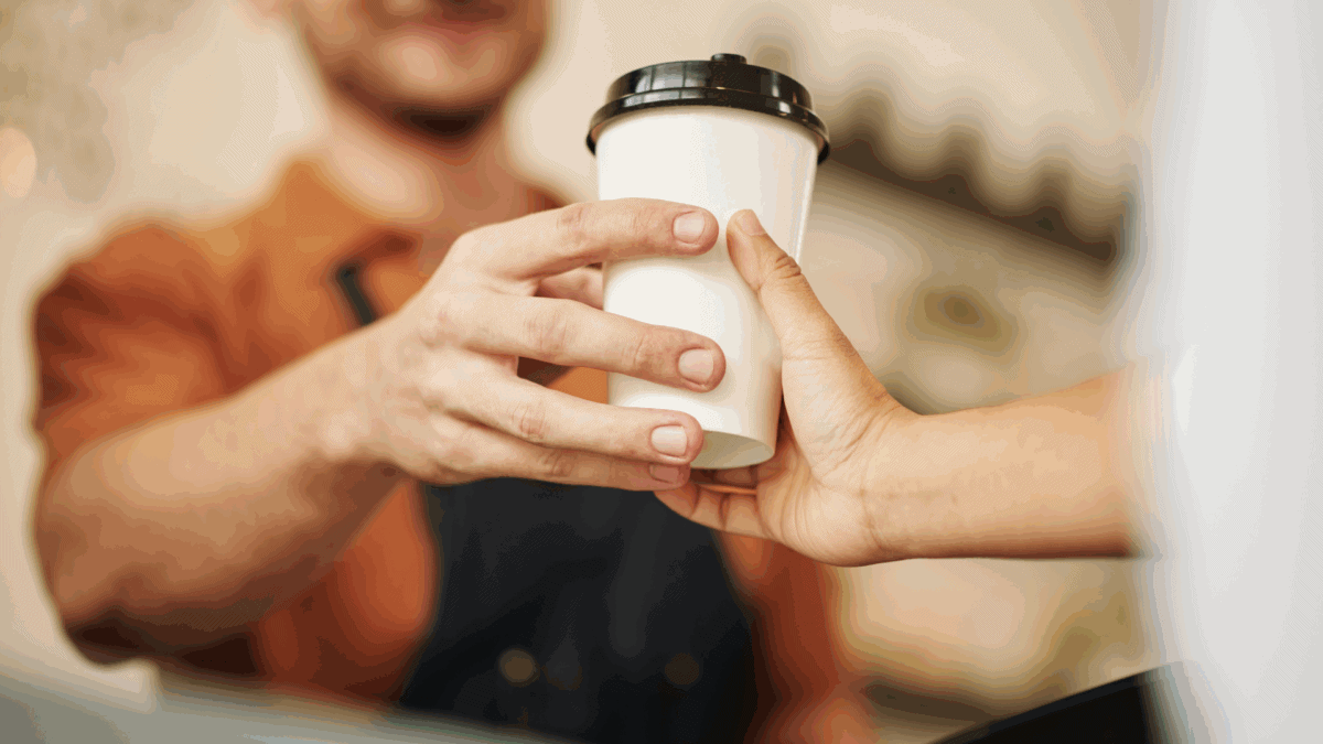 A close-up image of a man handing a disposable cup with a lid to a customer, exemplifying a retail customer experience.