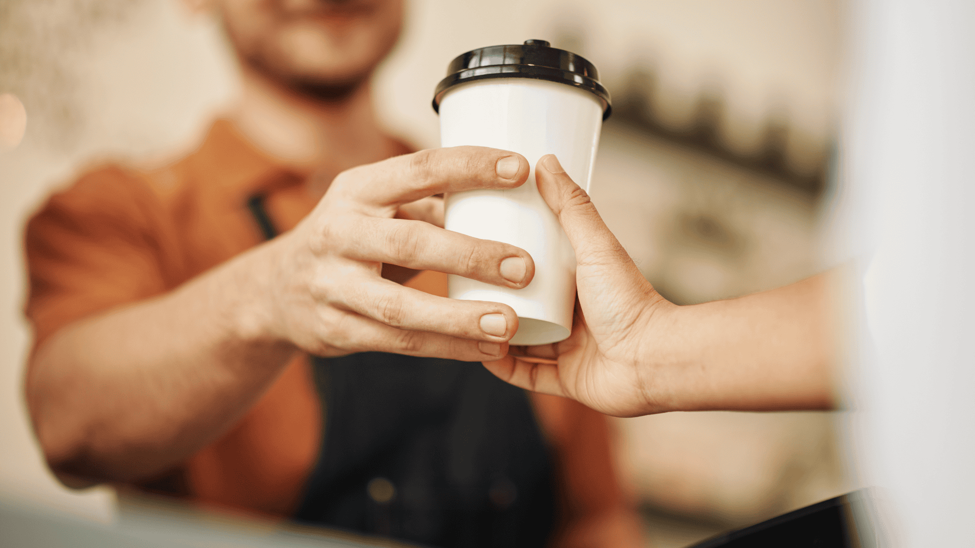 A close-up image of a man handing a disposable cup with a lid to a customer, exemplifying a retail customer experience.