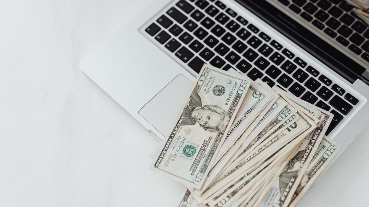 An overhead view of an open laptop with banknotes on the keyboard to discuss what is loss prevention in retail.