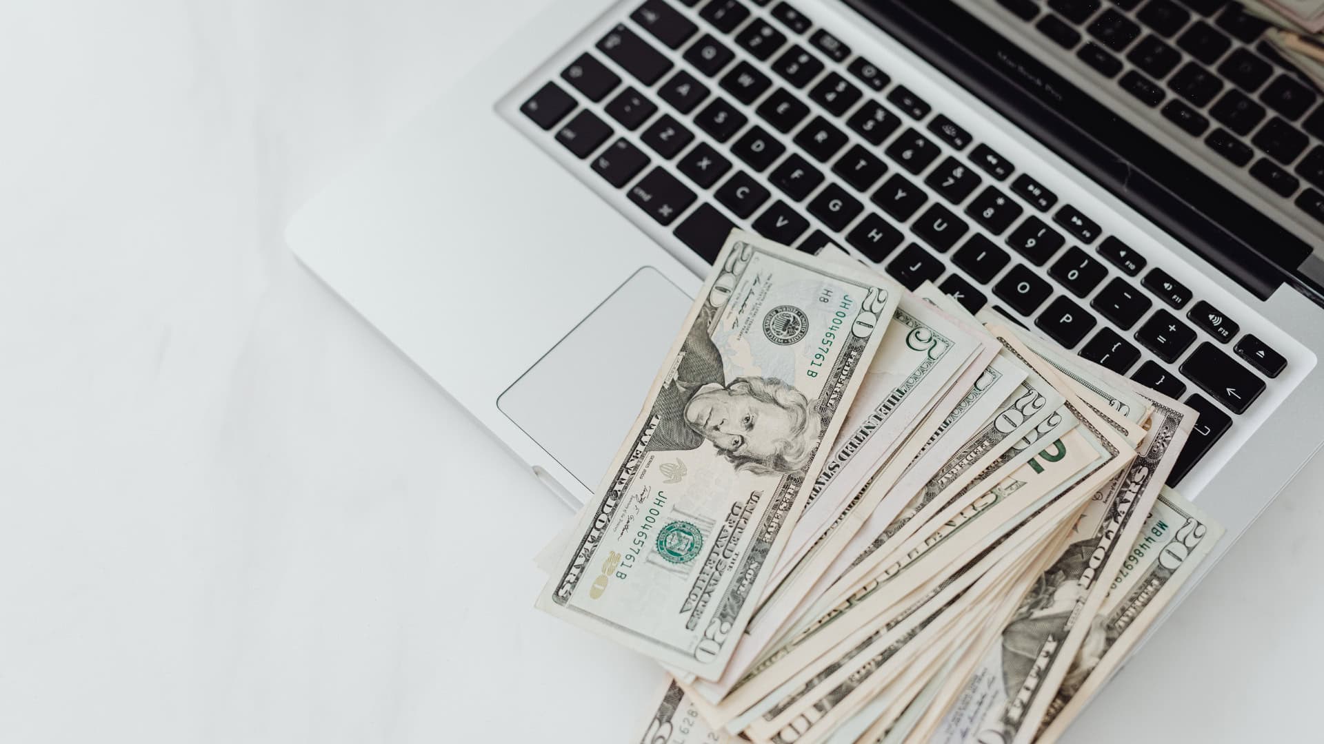 An overhead view of an open laptop with banknotes on the keyboard to discuss what is loss prevention in retail.