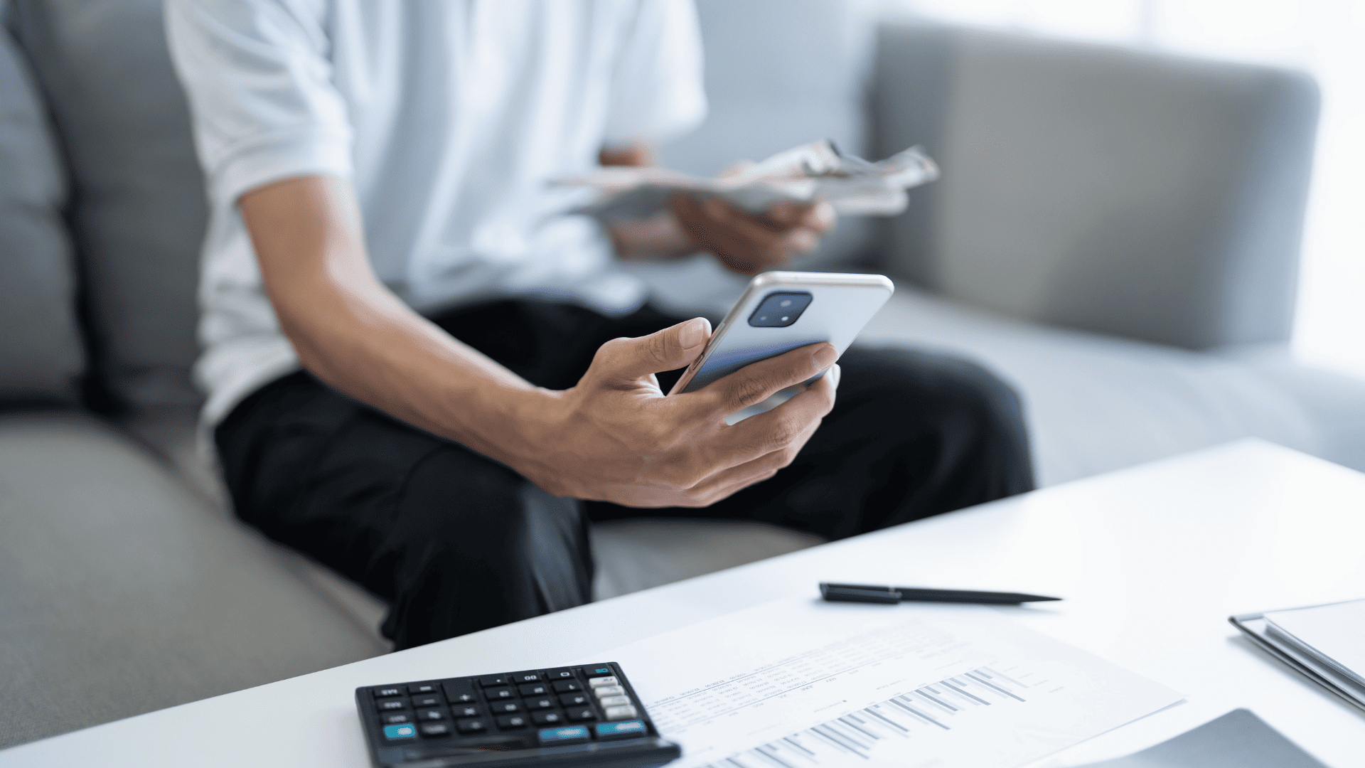 Image of a man sitting in an armchair, facing a table. The man is holding a cell phone in his hand to illustrate the ease of remote monitoring.