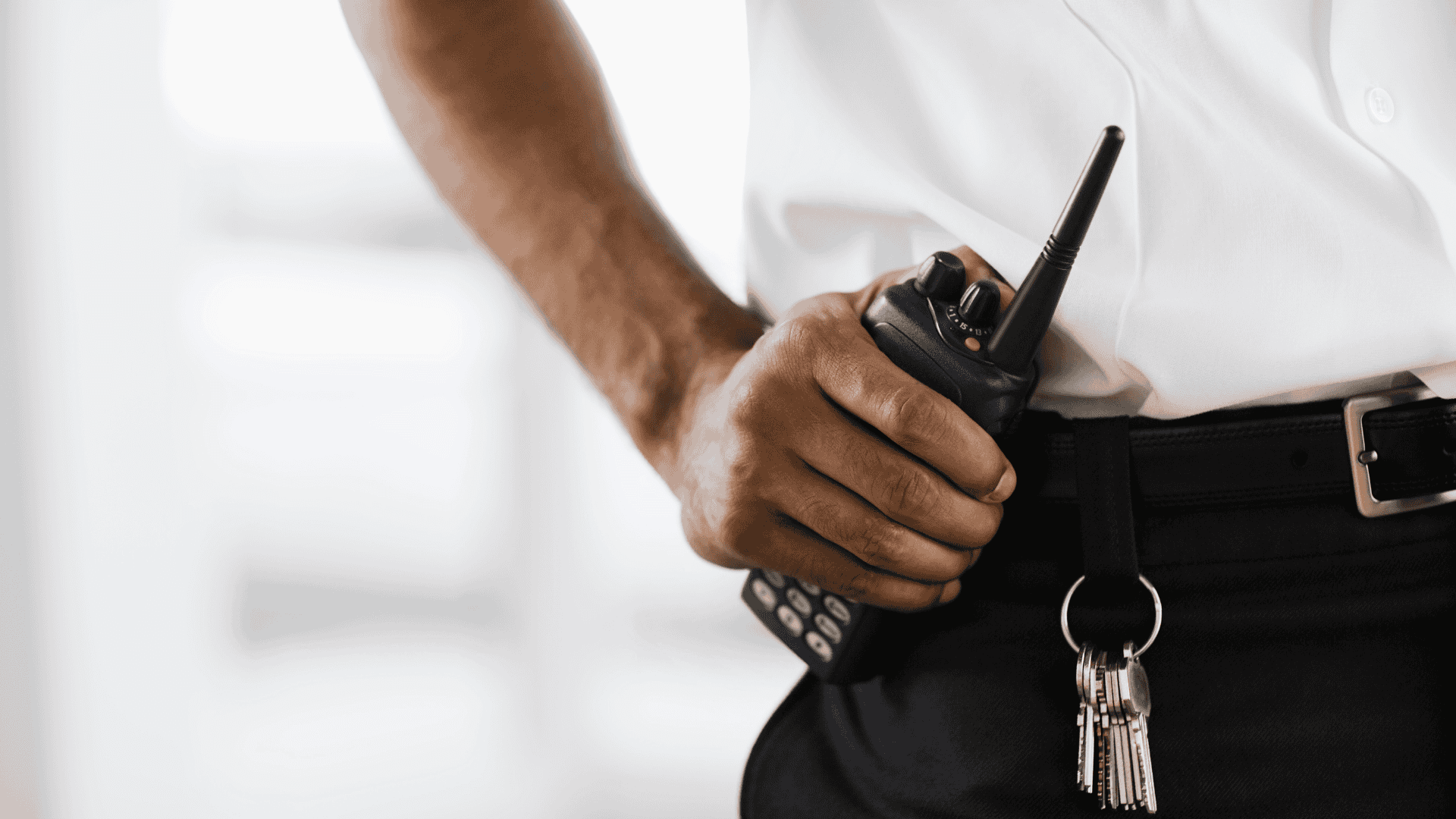 Close-up photo of a security guard holding his radio. This is a representation of physical security.