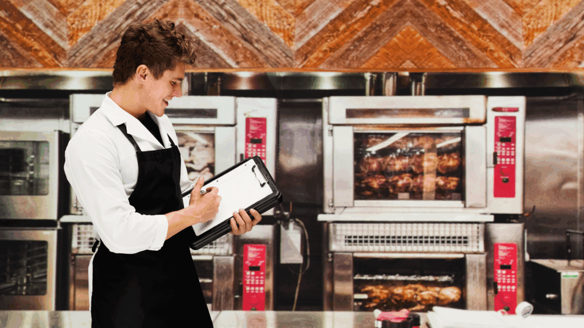 Image of a young man wearing a black apron and holding a clipboard reviewing a restaurant loss prevention checklist.