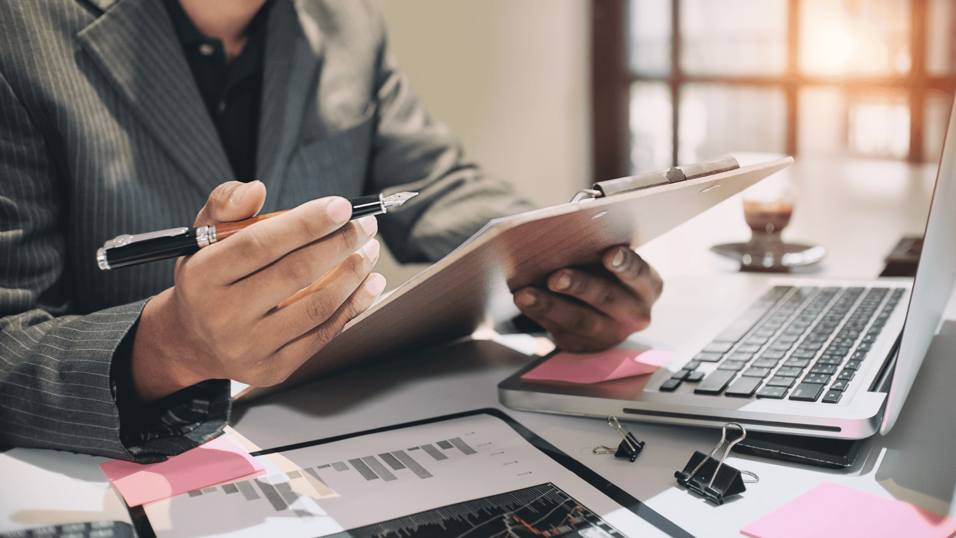 Close-up photo of a man holding a clipboard and a pen, reviewing the log of an audit trail.