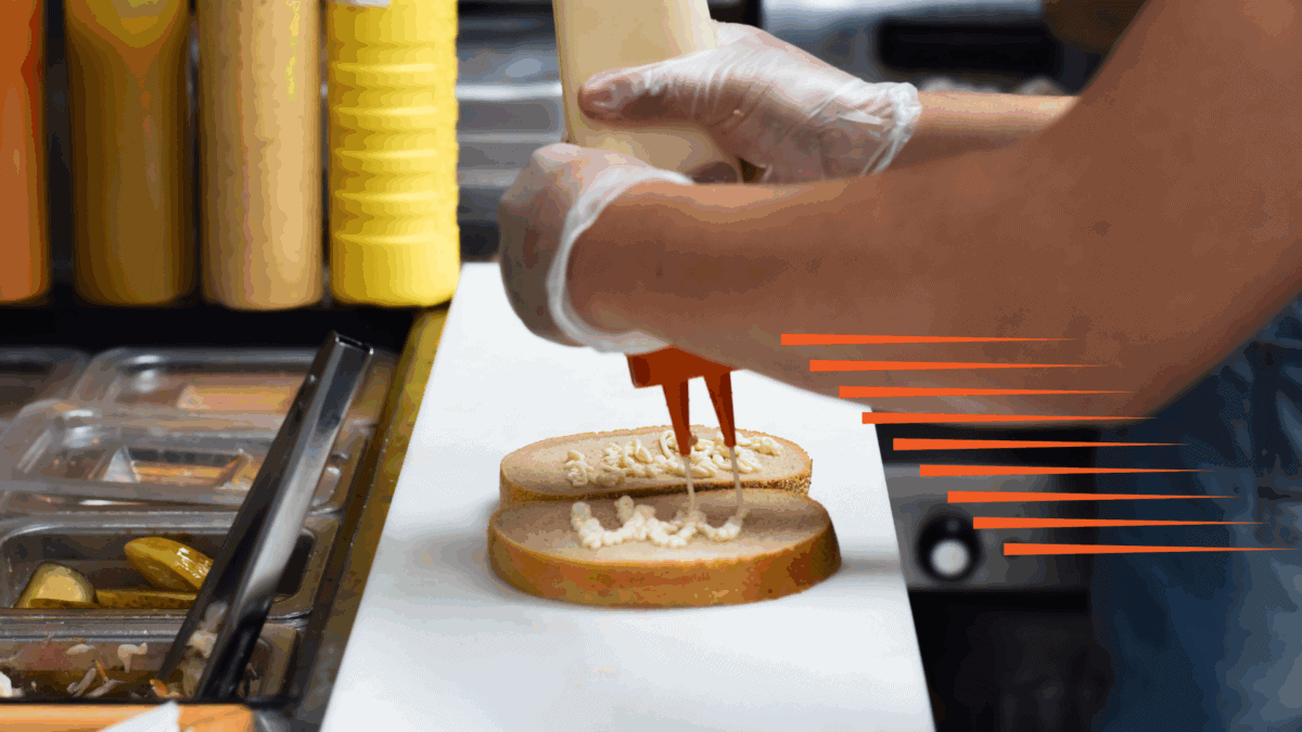 Close-up of a person putting dressing on a couple of pieces of bread as an example of QSR speed of service.