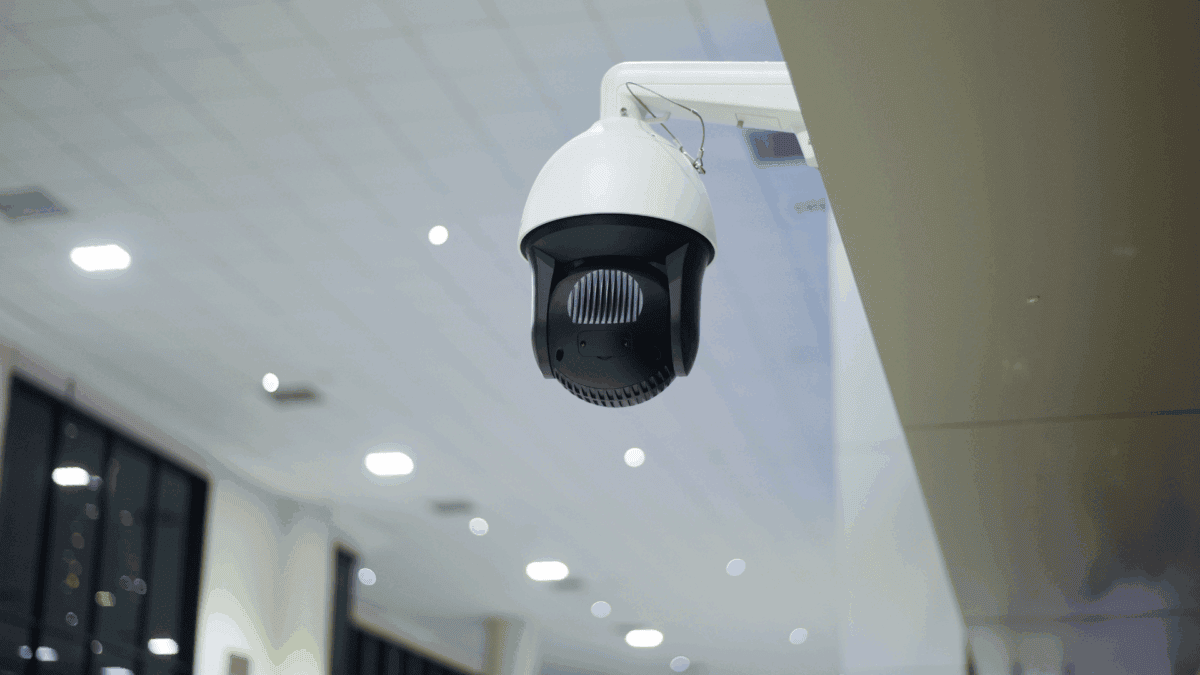 A ceiling-mounted security camera is shown inside a brightly lit building, highlighting surveillance technology often used in NVR vs DVR cameras comparisons.