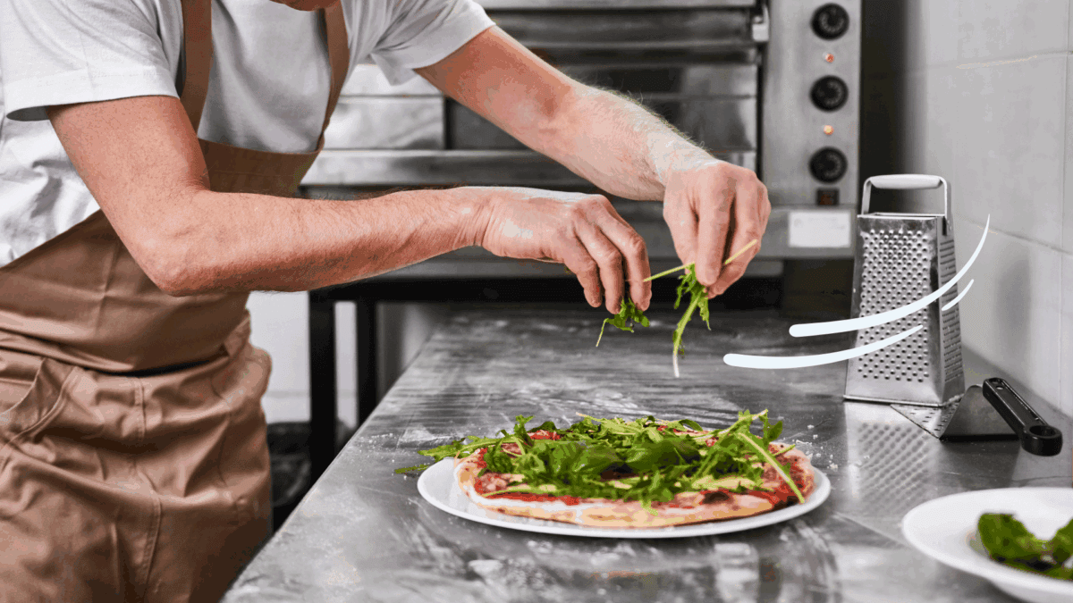 A close-up image of a man placing arugula on a pizza in an industrial kitchen as an example of how to improve speed of service in a restaurant.