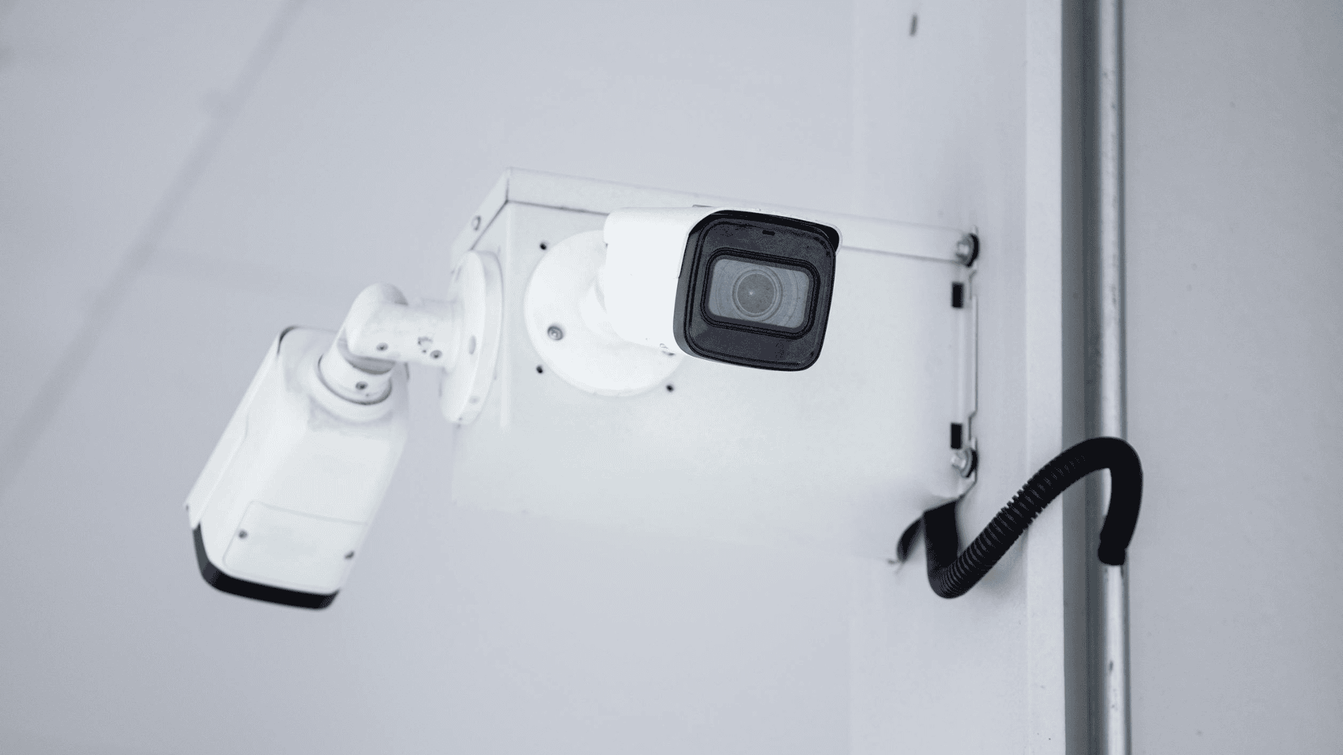 A close-up of a mounted white security camera with visible wiring, illustrating key features often compared in analog vs digital IP security cameras.