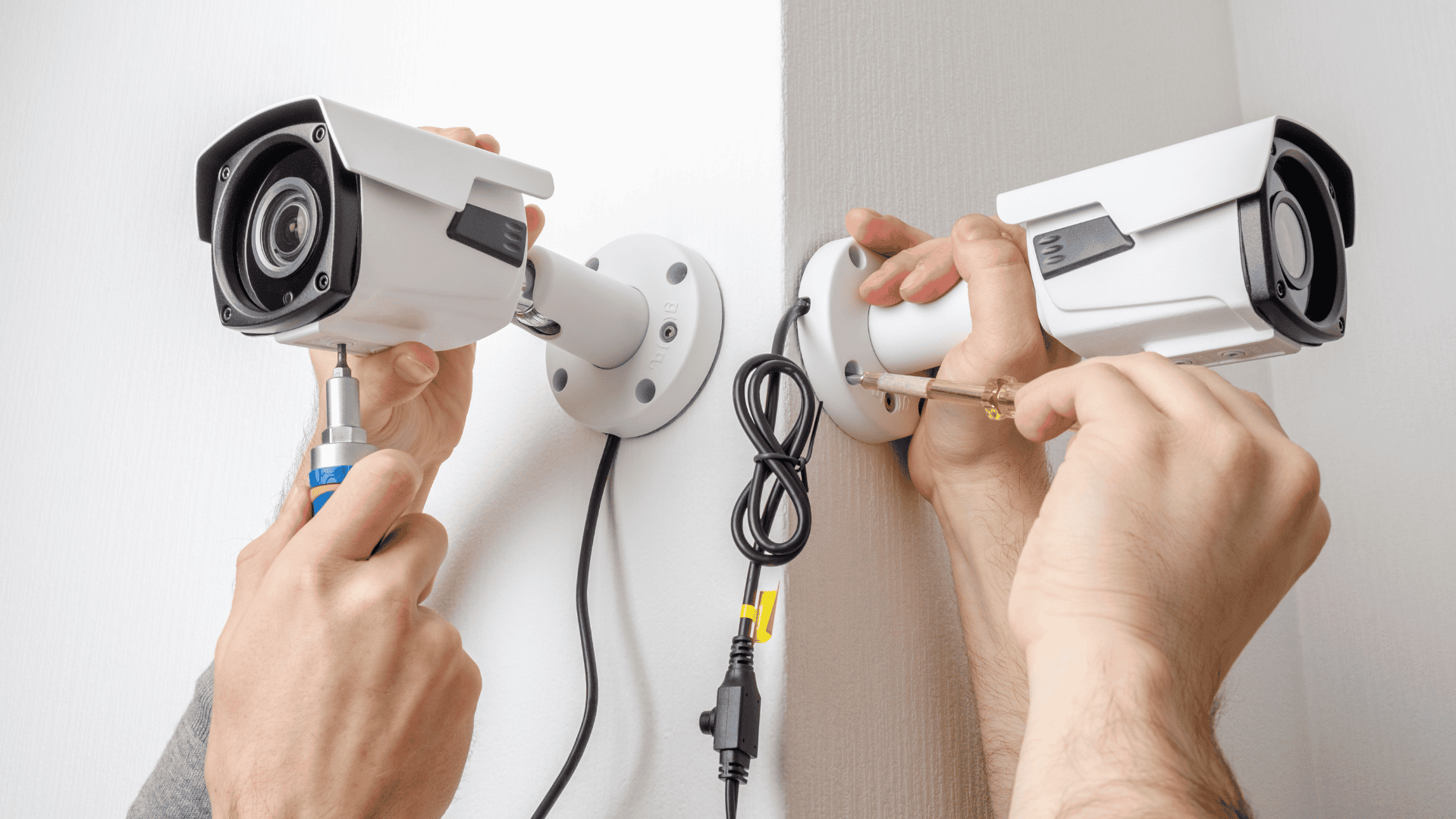 Two people install bullet-style security cameras on a corner wall, representing one of the many types of security cameras used for monitoring indoor and outdoor spaces.