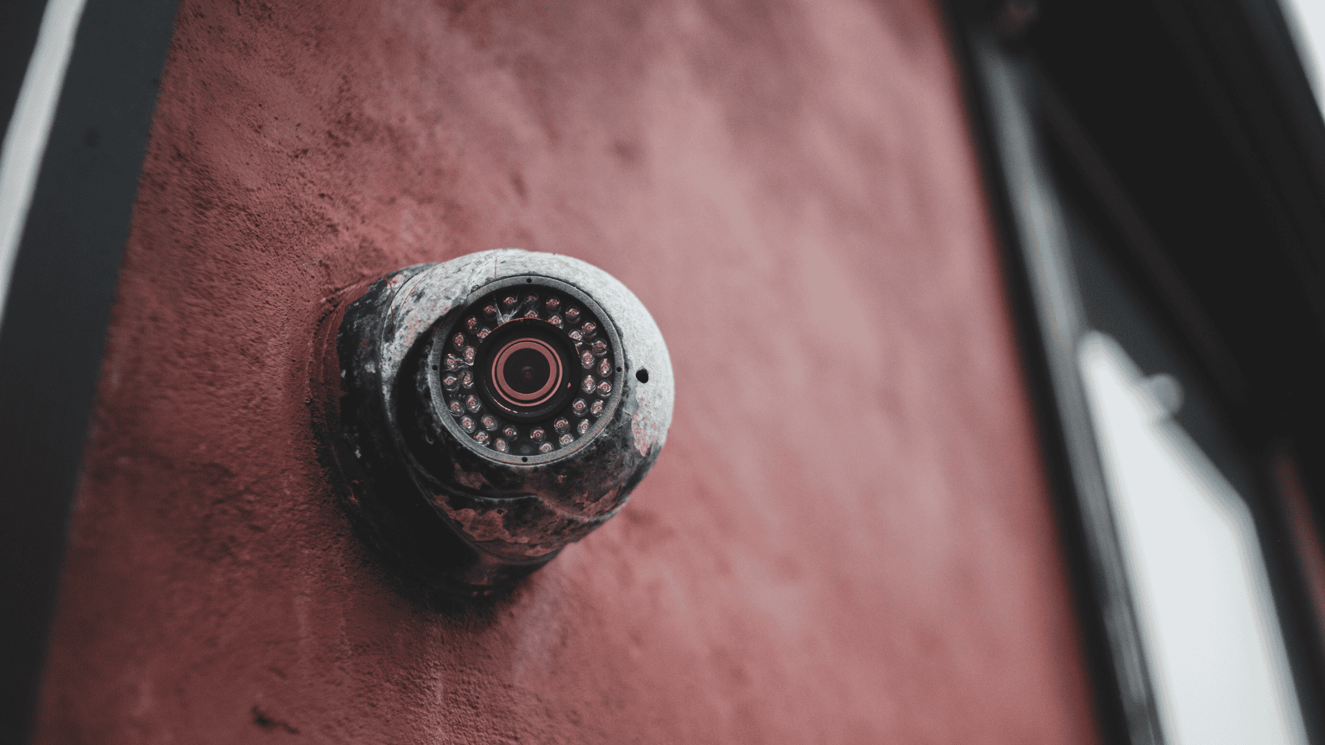 A weathered security camera mounted on a red wall symbolizes early surveillance technology, visually referencing the history of security cameras and their evolution over time.