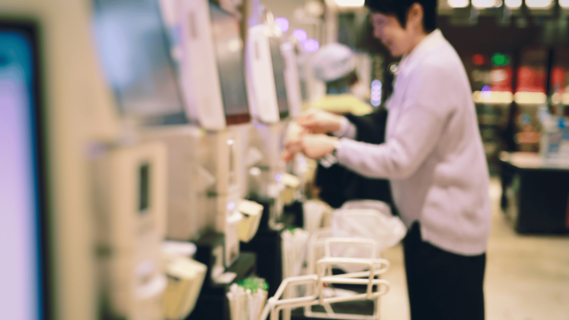 A person interacts with a self-service checkout kiosk in a retail environment, representing a common setting where self checkout theft can occur through item mis-scanning or intentional omission.