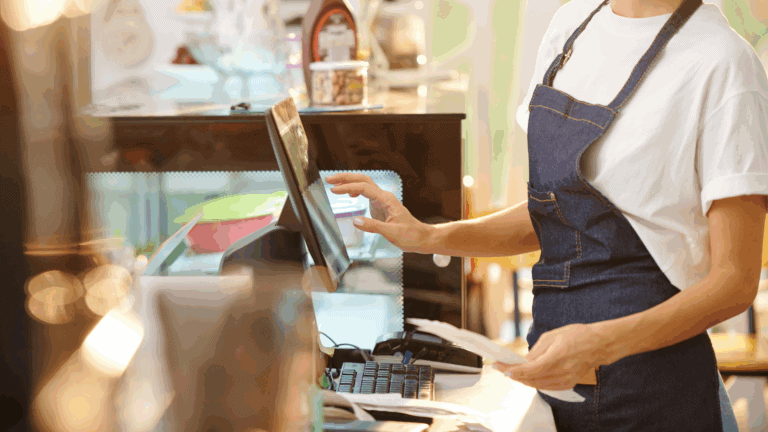 A retail worker in an apron operates a point-of-sale system while holding receipts, representing frontline roles in safeguarding store operations—an ideal visual for discussing loss prevention vs asset protection.