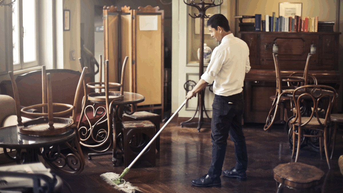 A man casually sweeps the floor in an empty restaurant, illustrating a subtle example of time theft in the workplace.