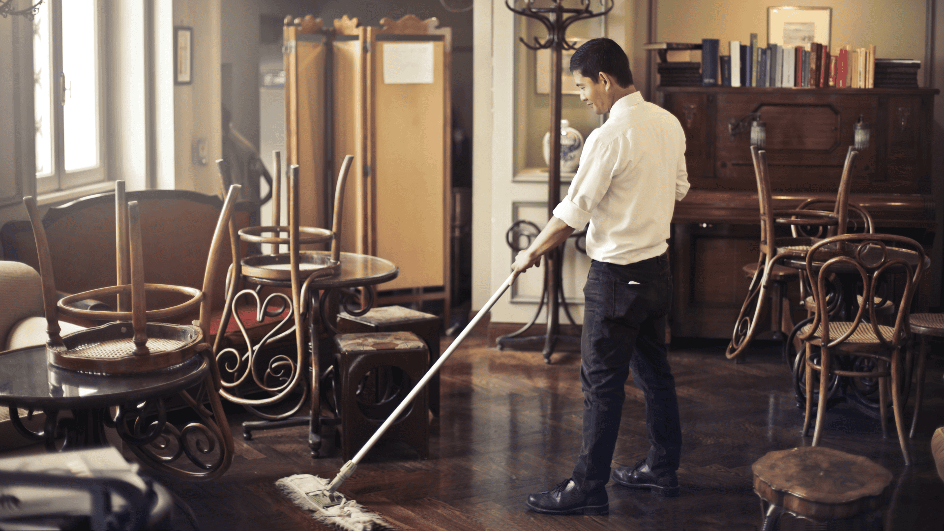 A man casually sweeps the floor in an empty restaurant, illustrating a subtle example of time theft in the workplace.