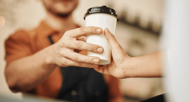 A close-up image of a man handing a disposable cup with a lid to a customer, exemplifying a retail customer experience.