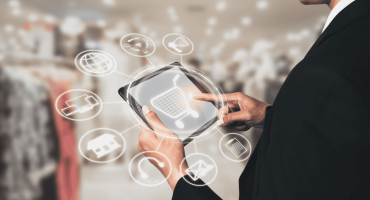 Image of a man in a department store holding a tablet. The tablet has a white illustration of a shopping cart in the center, and surrounding the tablet are various icons alluding to stores, shopping experiences, and retail safety.