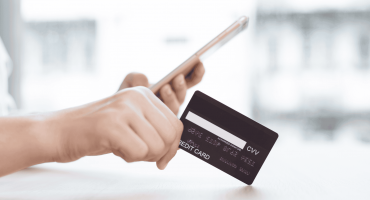 Image of a person's hands holding a cell phone in one and a credit card in the other as an example of QSR Loss Prevention.