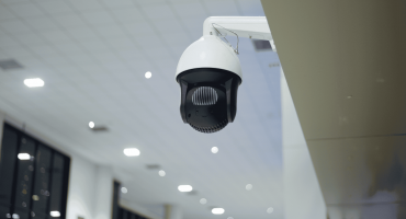 A ceiling-mounted security camera is shown inside a brightly lit building, highlighting surveillance technology often used in NVR vs DVR cameras comparisons.