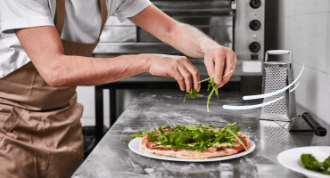 A close-up image of a man placing arugula on a pizza in an industrial kitchen as an example of how to improve speed of service in a restaurant.