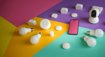 A modern AI security camera sits on a colorful background surrounded by smart home devices, light bulbs, and a smartphone, visually representing the interconnected ecosystem powered by an AI security camera.