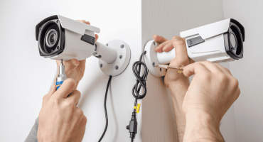 Two people install bullet-style security cameras on a corner wall, representing one of the many types of security cameras used for monitoring indoor and outdoor spaces.
