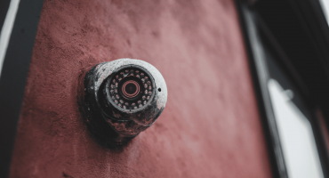 A weathered security camera mounted on a red wall symbolizes early surveillance technology, visually referencing the history of security cameras and their evolution over time.