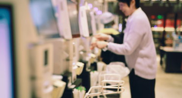 A person interacts with a self-service checkout kiosk in a retail environment, representing a common setting where self checkout theft can occur through item mis-scanning or intentional omission.