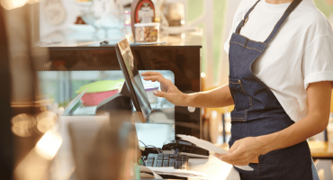 A retail worker in an apron operates a point-of-sale system while holding receipts, representing frontline roles in safeguarding store operations—an ideal visual for discussing loss prevention vs asset protection.