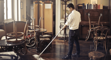 A man casually sweeps the floor in an empty restaurant, illustrating a subtle example of time theft in the workplace.